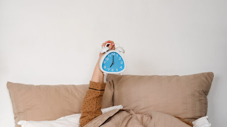 Hand holding alarm clock in bed. Good morning concept