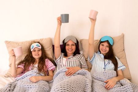 Happy family moment with mugs raised high in bed. Pajama Party. Girls' night out