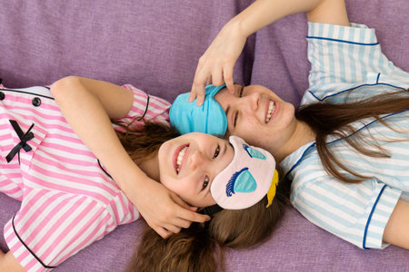 Sisters lying on the couch laughing with eye masks on. Family portrait