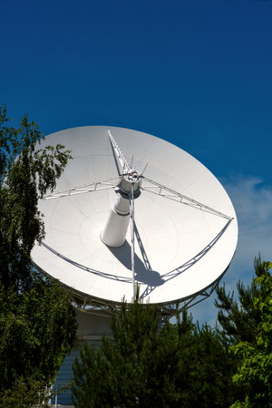 White radio telescope dish with trees and blue sky.