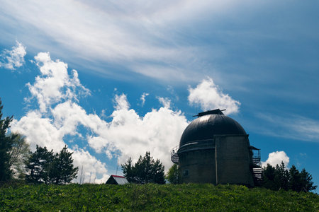 Brick observatory dome on a grassy hill with blue sky and clouds.