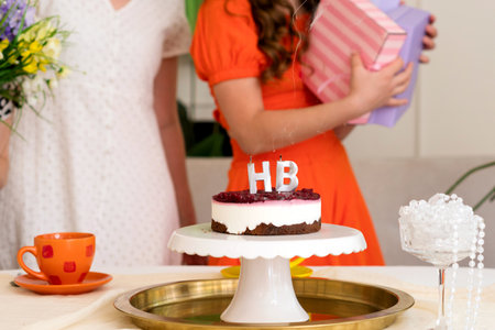 Young girl opening a gift at a birthday party, family watching. Cake and festive candles in the...