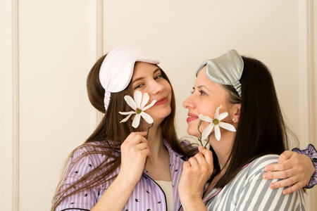 Mother and teenager daughter in striped pajamas holding flowers to their cheeks.の写真素材