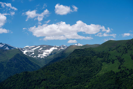 Snow-capped mountains and lush green valleys under bright blue sky.