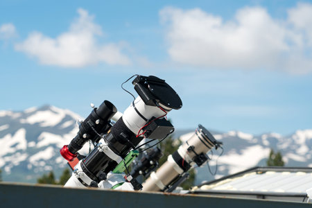 Telescopes on observatory rooftop with mountains and blue sky. Device used to observe distant objects for astronomyの写真素材