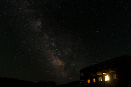 Milky Way galaxy above a brightly lit building at night. Astrophotography and nightscape