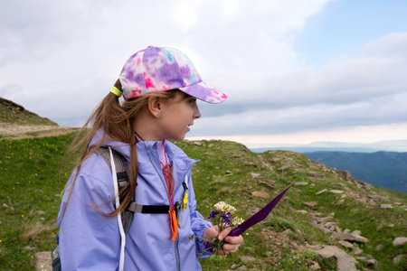 Girl holding flowers and a trowel, smiling with cloudy sky. Young Naturalist's Botanical Workshopの写真素材