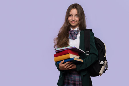 A smiling schoolgirl holds a stack of books while posing confidently.の写真素材