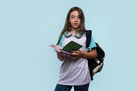 Surprised girl holding a notebook, wearing a backpack and headphones around her neck.