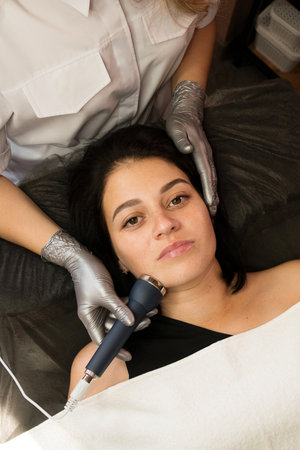 Close-up of a woman receiving phonophoresis ultrasound therapy on her face in a skincare session. Hardware anti-aging cosmetic procedureの写真素材