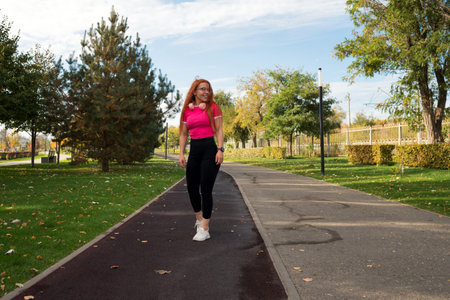 Woman walking in a park, wearing headphones and sportswear, enjoying a sunny day.の写真素材