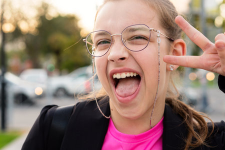 A playful girl giving a peace sign and yelling in excitement. Teenager taking selfies while walking down a city street in the eveningの写真素材