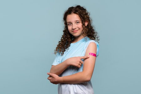 Smiling girl pointing at her raised arm with a pink bandage.の写真素材