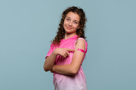 Girl pointing at a pink bandage on her arm after receiving a vaccine.の写真素材