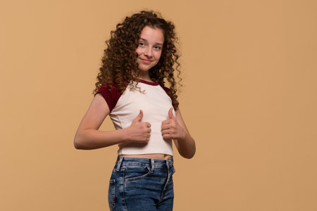 A young girl showing a thumbs-up pose, smiling confidently from a side angle against a beige background.の写真素材