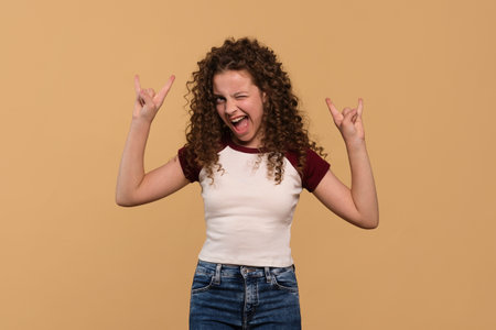 A young girl flashing rock hand signs with an enthusiastic expression against a beige background.の写真素材