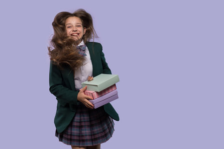 A laughing schoolgirl holds colorful gift boxes with her hair blowing in the wind. Girl is jumping for joyの写真素材