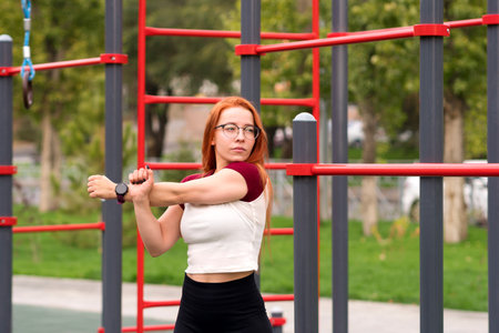 Woman performing arm stretches as part of her warm-up routine at an outdoor fitness area.