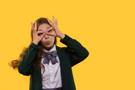 A playful schoolgirl making binoculars with her hands while posing.