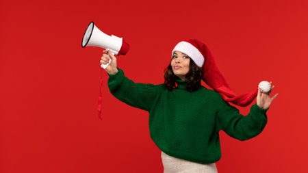 Confident woman in Santa hat raising a megaphone with a playful look.の写真素材