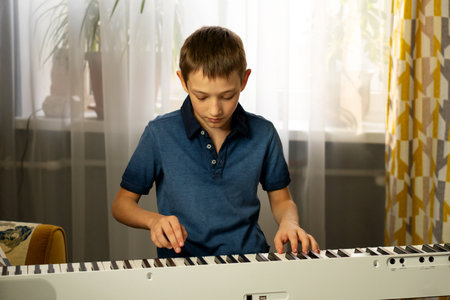 Boy in blue shirt playing piano near a window with curtains. Practicing piano at home. The concept of educationの写真素材