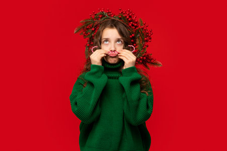Young girl in a green sweater making a playful mustache with candy canes, looking amused.の写真素材