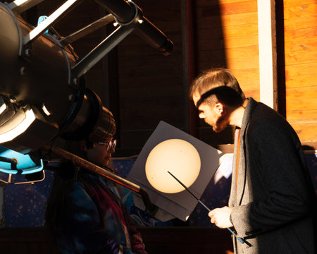 Man and girl examine a projected solar image from a telescope. Education activities, teaching,...