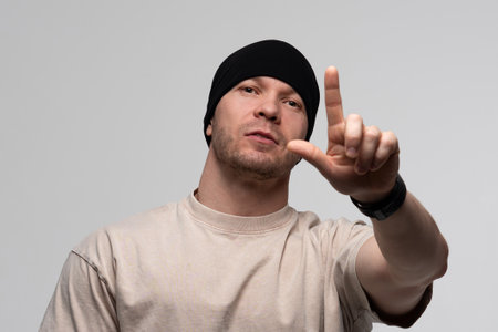 Man in black beanie and beige t-shirt pointing forward with intense expression.の写真素材