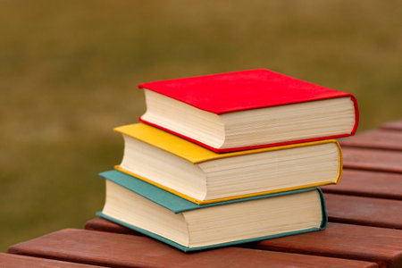 Stack of three colorful hardcover books on wooden bench outdoors.の写真素材