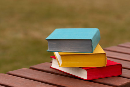 Colorful hardcover books stacked outdoors on wooden park bench.の写真素材