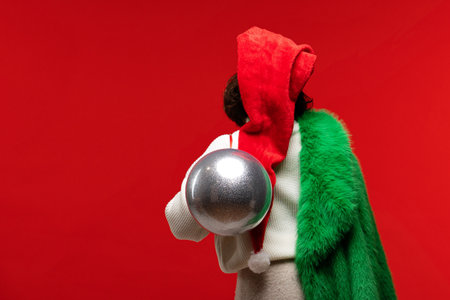 Back view of a woman in a festive outfit carrying a large silver ornament.の写真素材