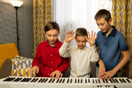 Three boys having fun while experimenting with the piano keys. Practicing piano at home. Education, teaching, learning and friendship concept.の写真素材
