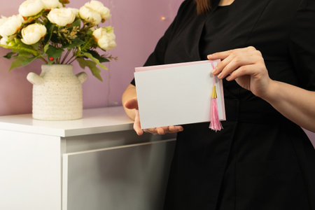 Close-up of woman's hands presenting blank decorative greeting card. Gift certificate for face and body treatments in the hands of cosmetician. Beauty and aesthetic health conceptの写真素材