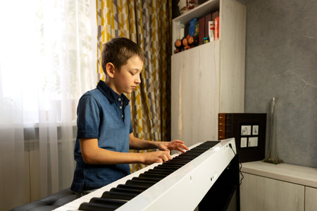 Side view of boy playing digital piano near a bookshelf. Practicing piano at home. The concept of educationの写真素材