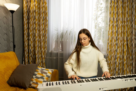 Girl in glasses playing piano with focus in a warmly decorated home. Learn piano at home. The concept of educationの写真素材