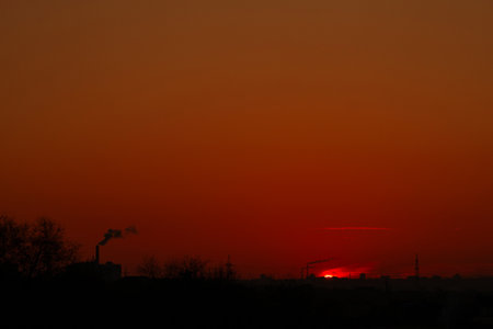 Fiery red sun dipping below horizon with industrial smokeの写真素材