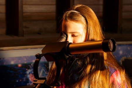 Young girl observes through solar telescope, illuminated by warm light