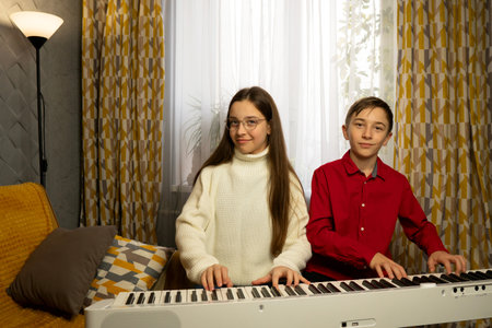 Two children playing a digital piano together in a cozy room setting. Learn piano at home. The concept of education, teaching, learning and friendship.の写真素材