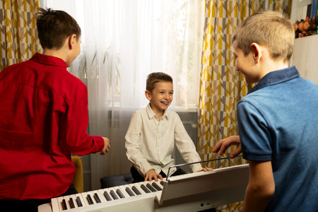 Smiling boy playing the piano while two friends watch. Practicing piano at home. Education, teaching, learning and friendship concept.の写真素材