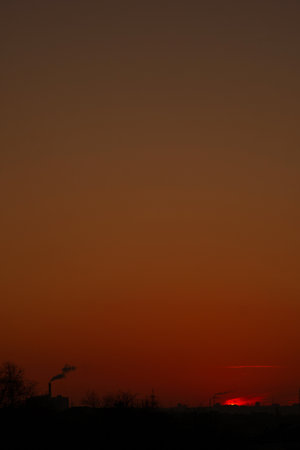 Dark orange skyline with factory smoke at twilight hourの写真素材