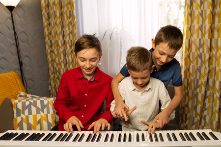 Three boys having fun at the piano, helping each other play. Practicing piano at home. Education, teaching, learning and friendship concept.の写真素材