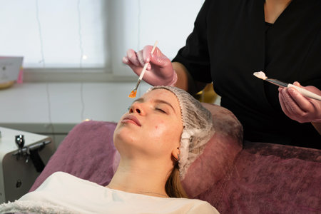 Esthetician applies hydrating facial mask to client in spa. Beauty treatment. Final stage of oxygen jet peeling. Girl enjoying skin rejuvenation therapy at cosmetology center.の写真素材