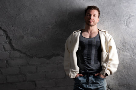 Man in a fleece hoodie and jeans leaning against a textured gray wall.の写真素材