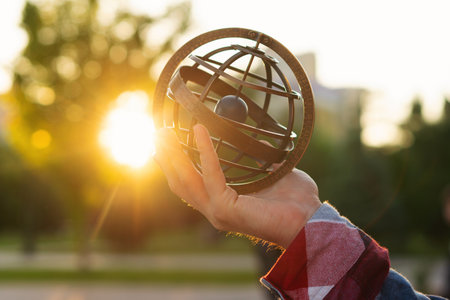 Hand holding antique metal globe against sunset in park. Armillary sphere on hand, spherical...