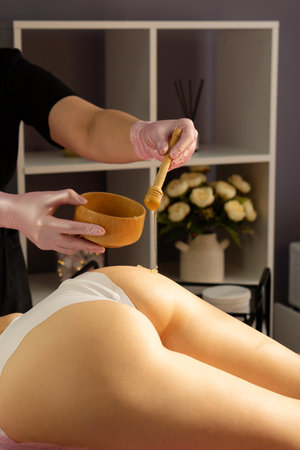 Beautician applying honey treatment to gluteal area during spa session. Honey detox massage or caramel liposuction.の写真素材