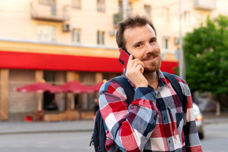 Smiling young man talking on phone in urban setting. Guy talking on smartphone outdoors. Concept of digital communication, connection and casual lifestyle.の写真素材