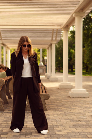 Young woman wearing stylish outfit stands outdoors under pergola.の写真素材