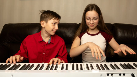 Boy in red shirt playing the piano, smiling at girl beside him. Practice piano at home. Concept of education, teaching, learning and friendship.の写真素材
