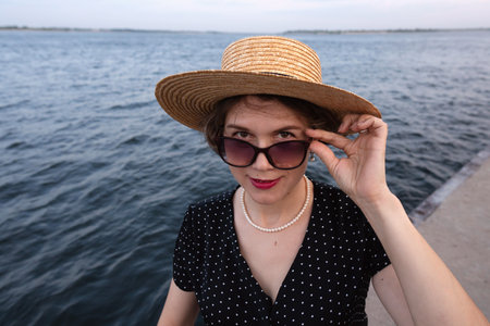 Close-up of stylish woman lifting sunglasses with gentle smile.の写真素材