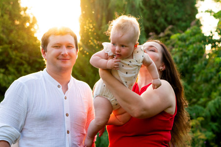 Dad smiles at camera while mom hoists their glowing, rimâ€‘lit baby between them; dust sparkles...